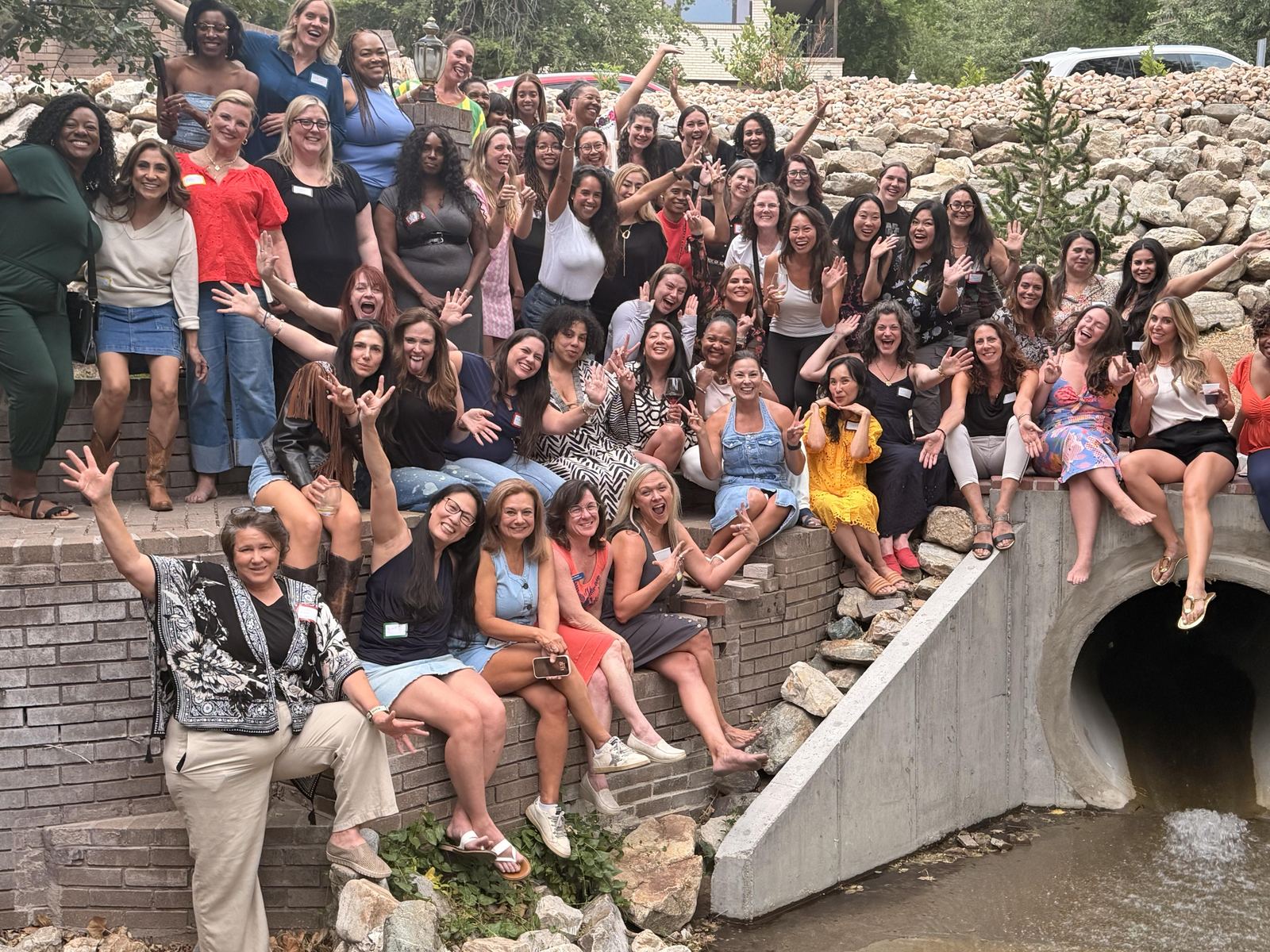 The Women Build AI community gathered on brick steps beside a creek, waving and laughing together.